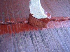 屋根に刷毛で下塗り材を塗る